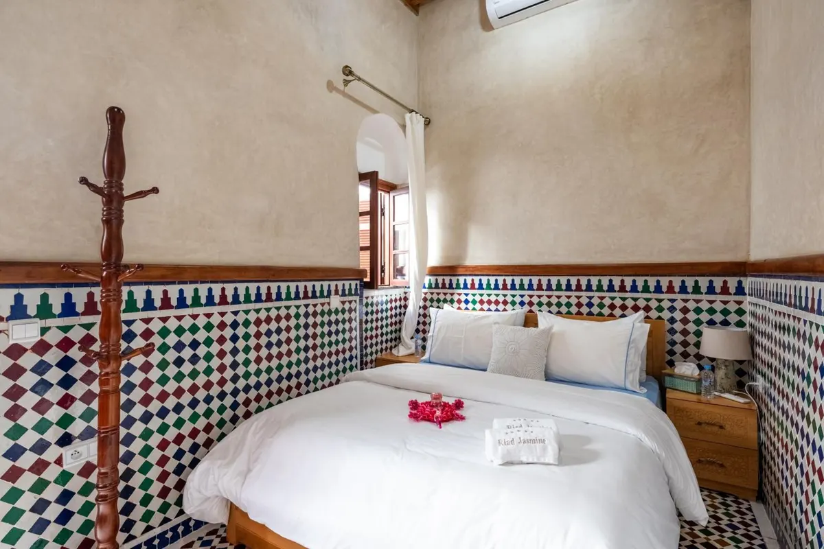 A bedroom with rose petals on the bed and zellige walls
