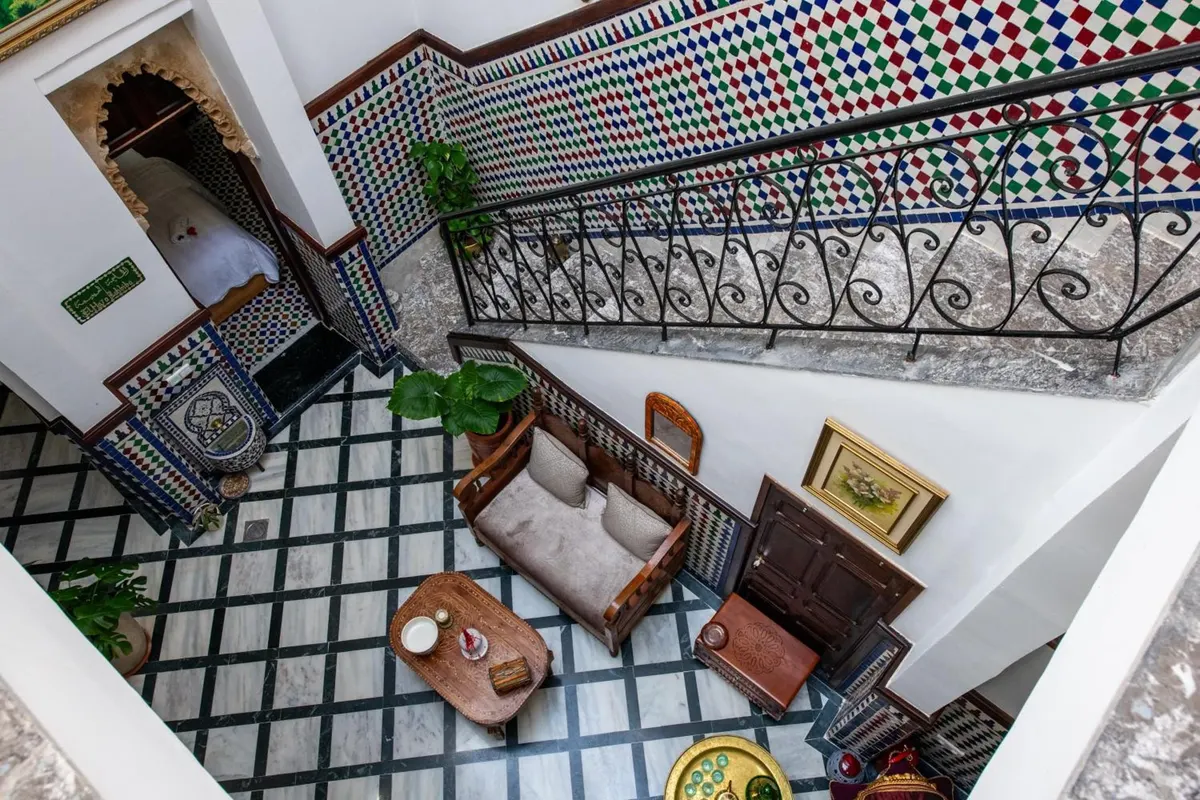 The patio of Riad Jasmine seen from the stair: zellige wall, wrought-iron balustrade and black-and-white marble floor