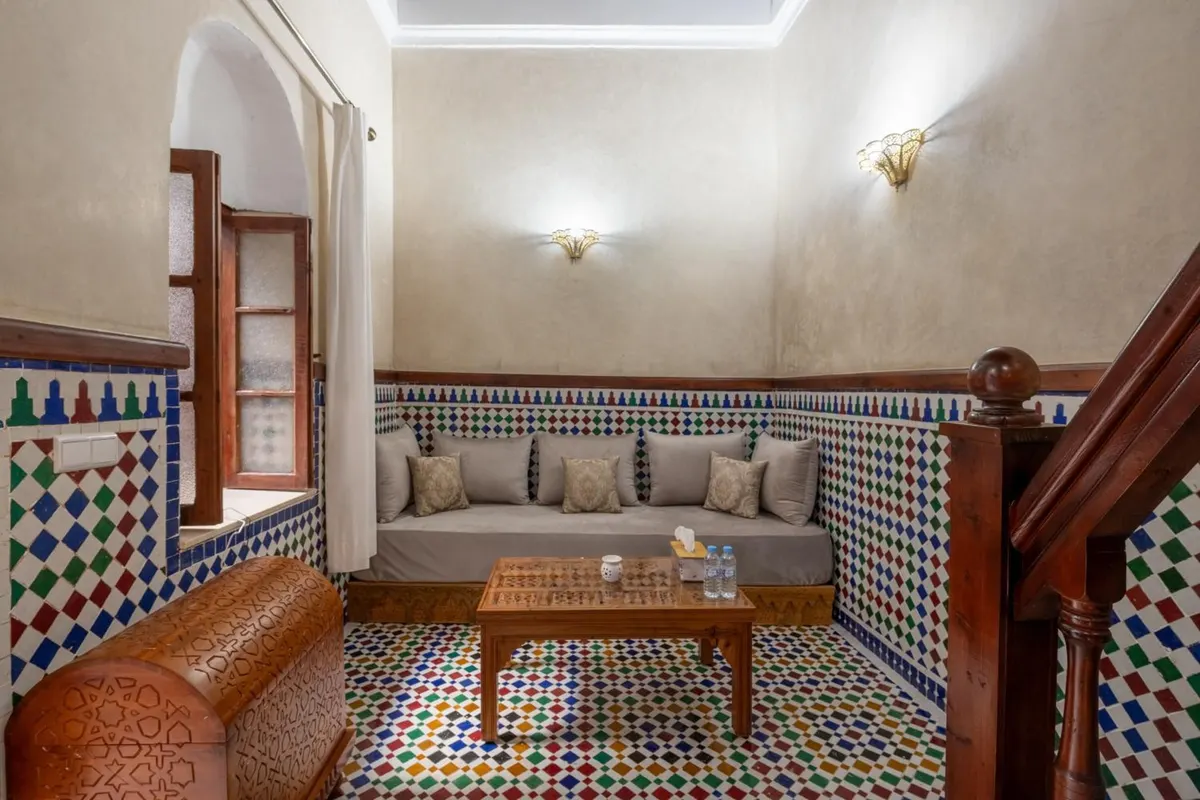 Lounge with banquette sofa, coloured zellige floor and carved chest