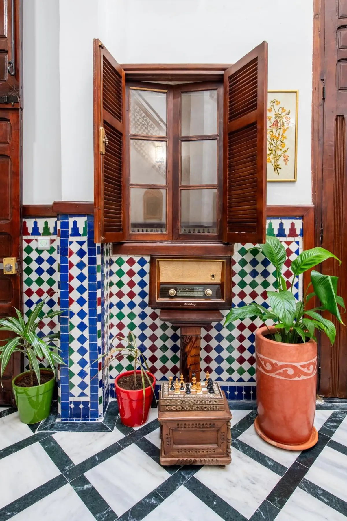 Carved wooden shutters above a zellige dado and potted plants