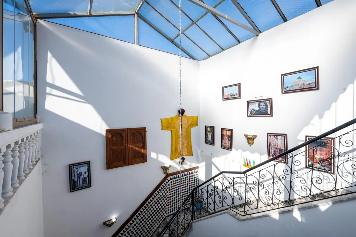 The stair under the glass roof, with framed pictures and a yellow caftan on the wall