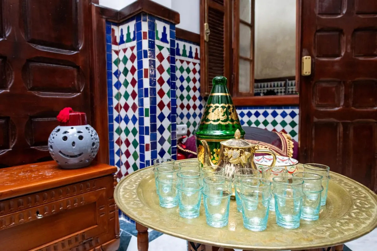 Brass tray with tea glasses and a green teapot between carved dark-wood cabinets