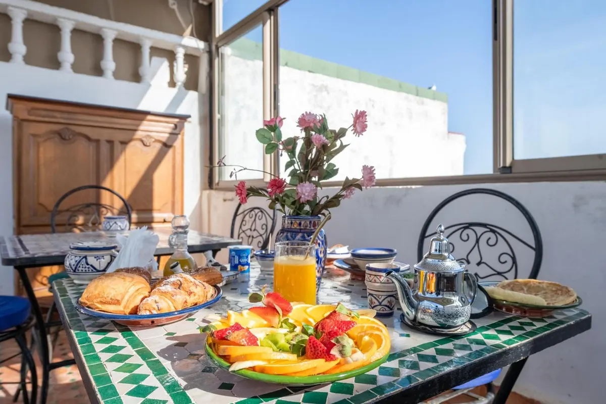 Breakfast on a green zellige table: breads, flatbreads, fruit, jams and tea