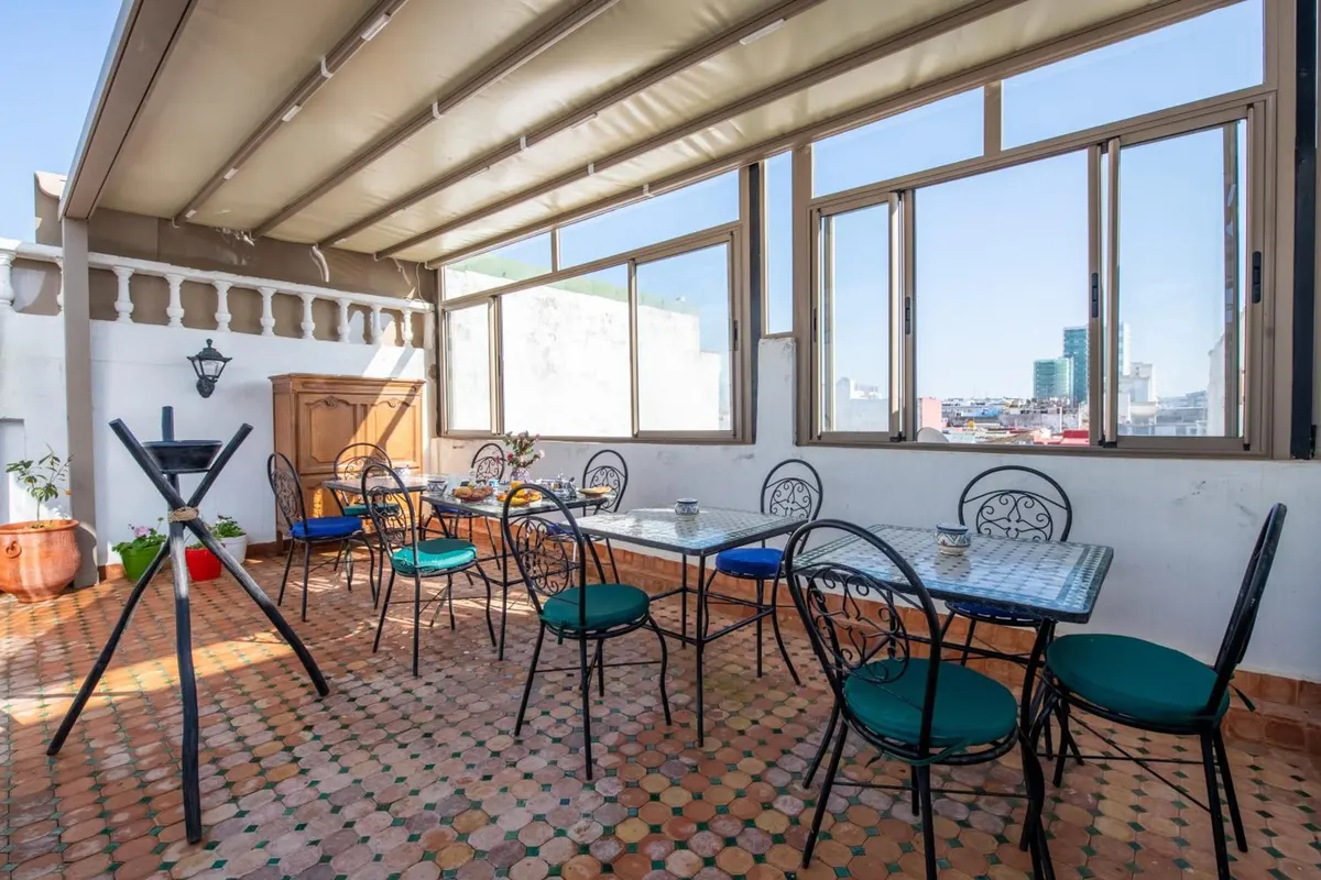 The roof terrace where breakfast is served: mosaic tables, iron chairs, awning and open sky